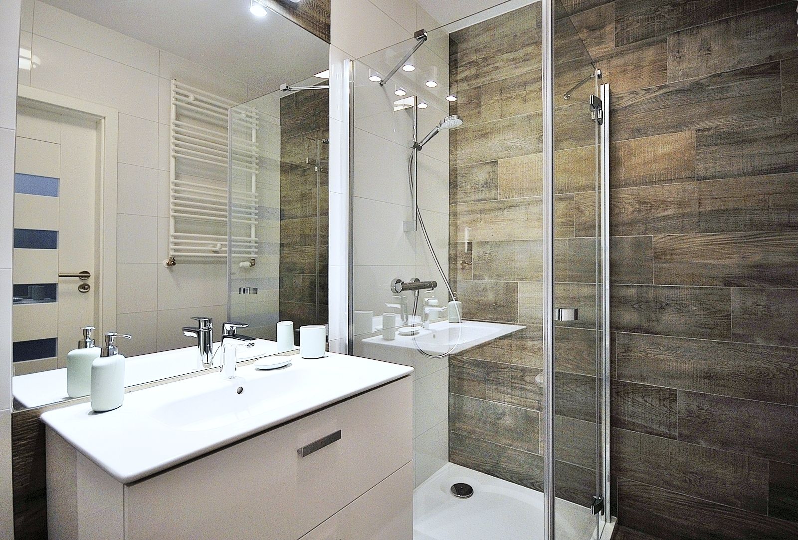 Un baño moderno con cabina de ducha de vidrio, tocador blanco con espejo y un perchero para toallas.
