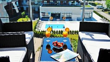 Un balcon avec des fauteuils en osier, une table avec deux verres de jus d’orange, un saladier rempli de fraises et un magazine.