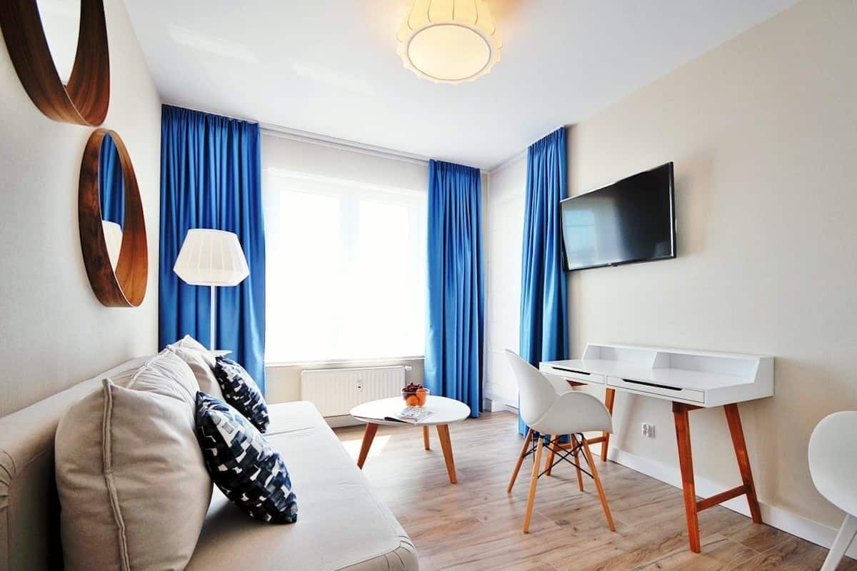 Ein modernes Wohnzimmer mit einer Couch, einem Esstisch, Stühlen, einem Fernseher und blauen Vorhängen.