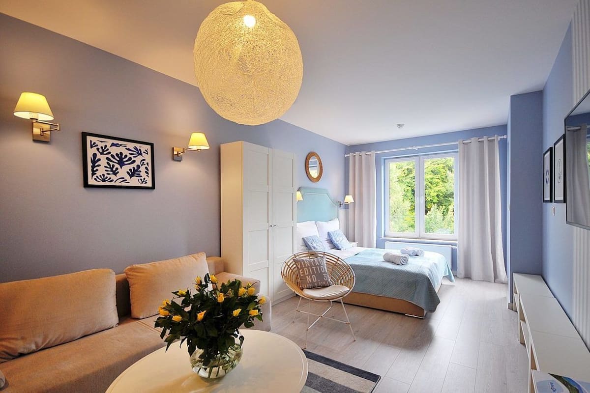 Ein modernes Schlafzimmer mit einem Bett, einem Schlafsofa, einem Sessel und einem Tisch mit Blumen.