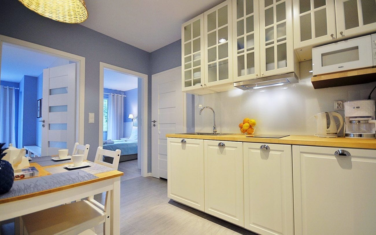 Een moderne keuken met witte kasten, een houten aanrechtblad en een magnetron. Achtergrond toont een eethoek met een tafel en stoelen.