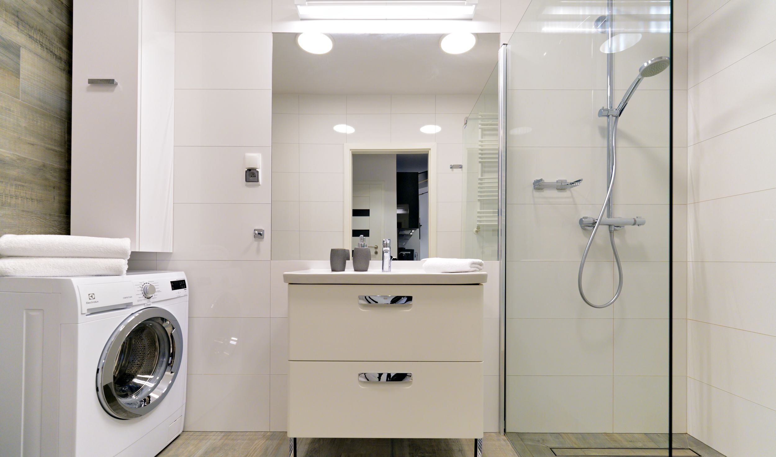 A modern bathroom with a glass-enclosed shower, a built-in washing machine, and a vanity with a mirror.