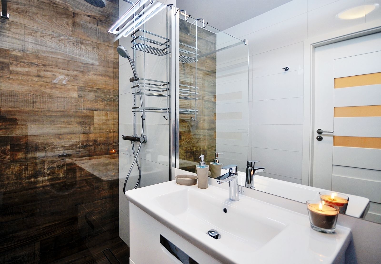 A modern bathroom with a large mirror, a white sink, a glass shower enclosure, and a wooden wall.