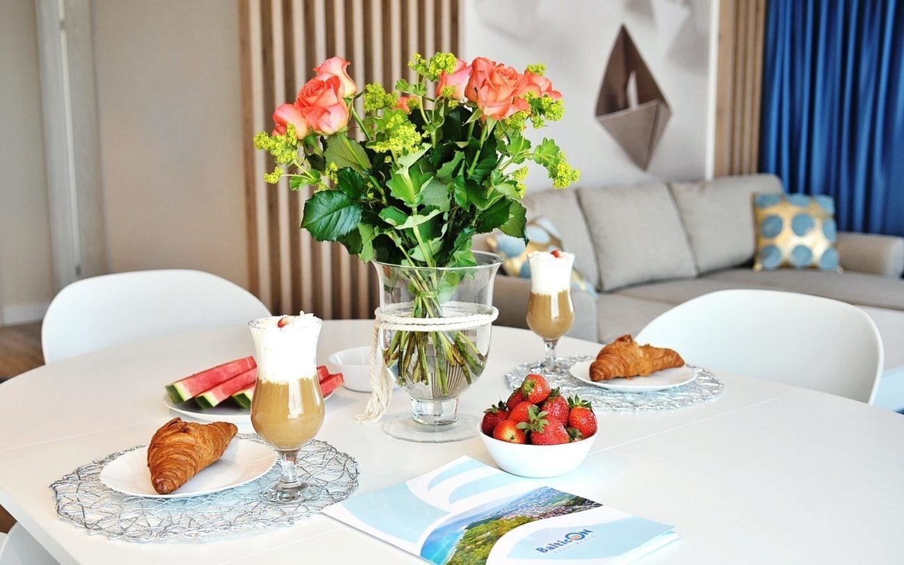 Et spisebord dækket med croissanter, en skål jordbær, et glas kaffe og en vase med blomster.
