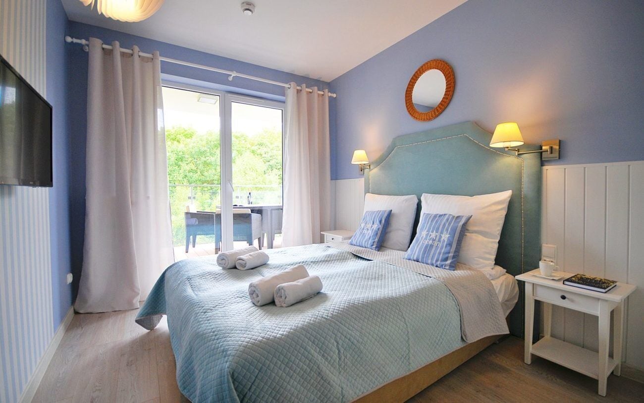 A bedroom with a large bed, two bedside tables, a TV, and a view of the outdoors.