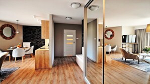 Un salon moderne avec un plancher en bois, un coin repas doté d’une table ronde et une cuisine avec un crédence noire.