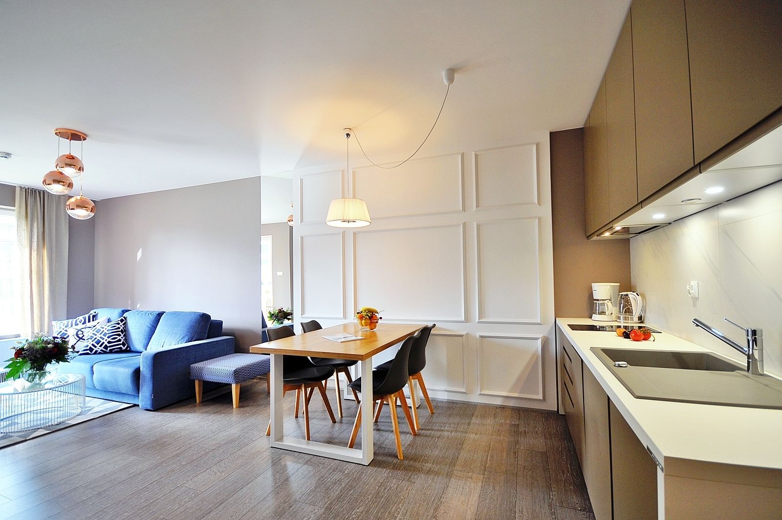 A modern living room with a blue sofa, a dining table with chairs, and a kitchen area with a sink and countertop.