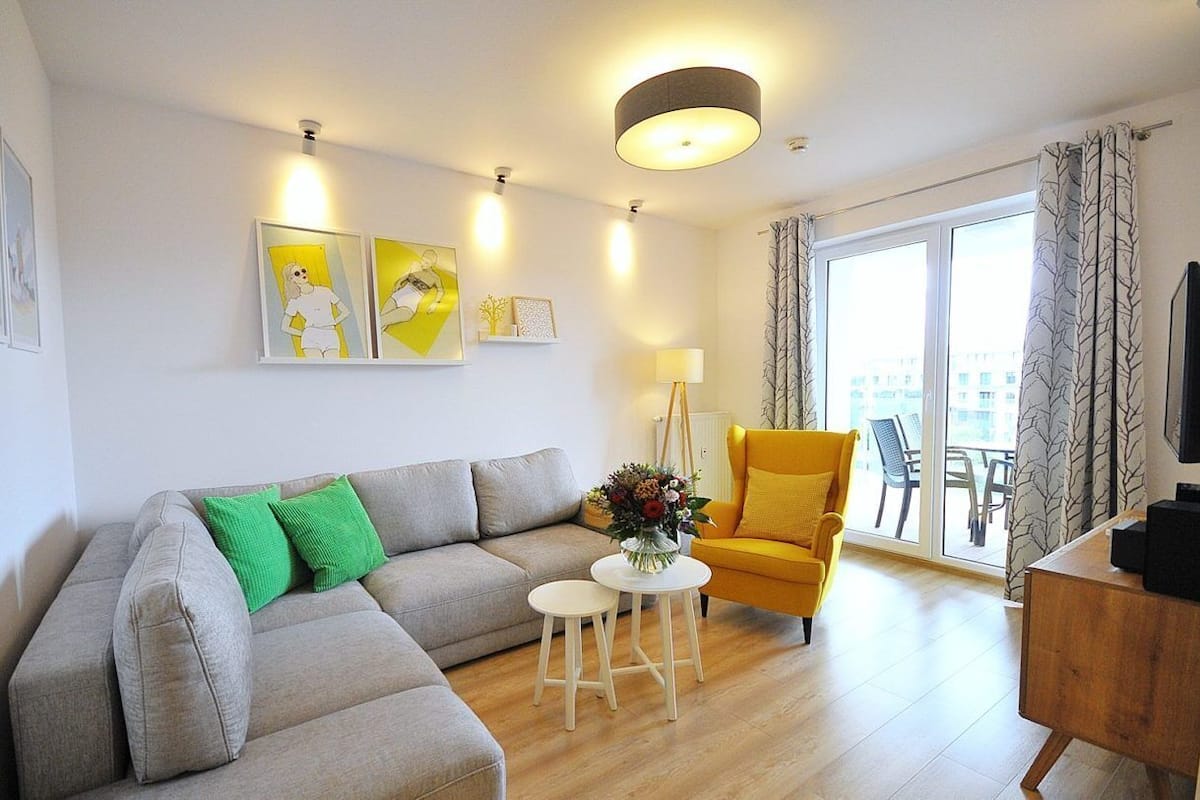 Ein modernes Wohnzimmer mit einem grauen Sofa, einem gelben Sessel und einem kleinen weißen Tisch mit einer Blumenvase.
