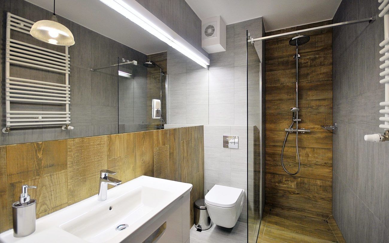Un baño moderno con un espejo grande, un lavabo blanco, un inodoro y una zona de ducha con mampara de vidrio.