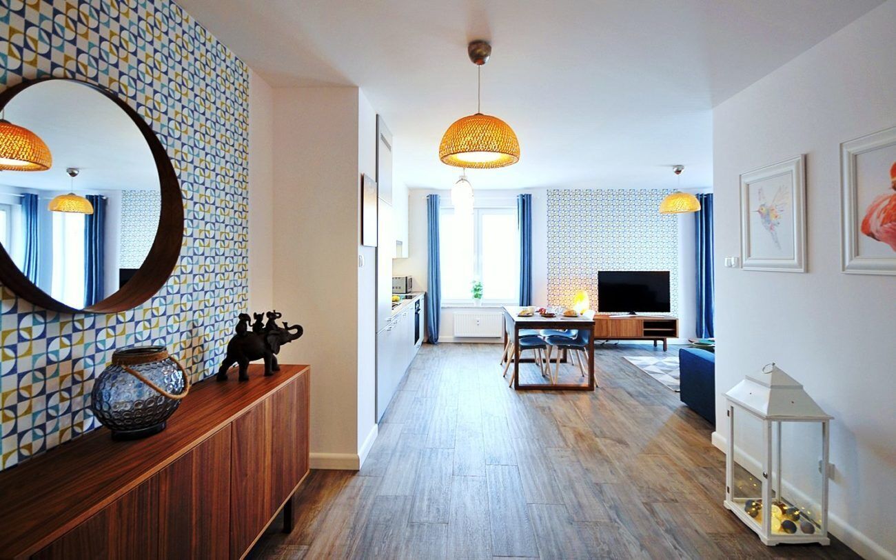 A modern living room with a wooden floor, a dining area, and a kitchen in the background.