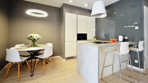Une cuisine moderne dotée d’un îlot central, de tabourets de bar blancs et d’un coin repas avec une table ronde et des chaises.
