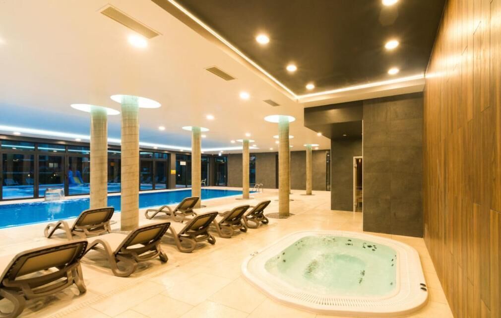 Zona de piscina interior moderna con sillones de descanso y un jacuzzi.
