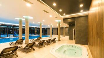 Zona de piscina interior moderna con sillones de descanso y un jacuzzi.