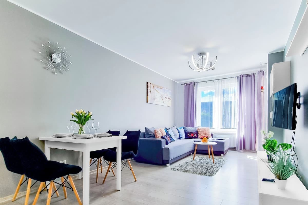 Ein modernes Wohnzimmer mit Essbereich, einem grauen Sofa, einem Fernseher und einer Kandelaber.