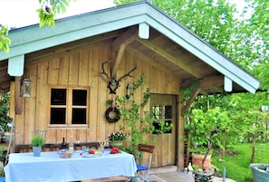 Eine rustikale Holzhütte mit überdachter Veranda, einem Esstisch gedeckt mit Speisen und Getränken sowie einer Bank.