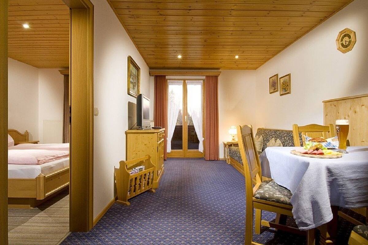 Hotelkamer met een houten plafond, een bed, een bureau met een computer, een eettafel met een maaltijd en uitzicht door een deur.