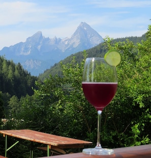 Un verre de vin rouge, agrémenté d’une tranche de citron vert, devant un paysage de montagne.
