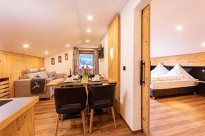 Une pièce chaleureuse avec un plancher en bois, une table à manger avec des chaises, un canapé et un lit doté d’une tête de lit en bois.
