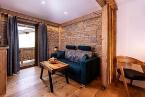 Une pièce chaleureuse avec un mur en pierre, un canapé bleu, une table en bois sur laquelle sont disposés des fruits, et une chaise en bois.