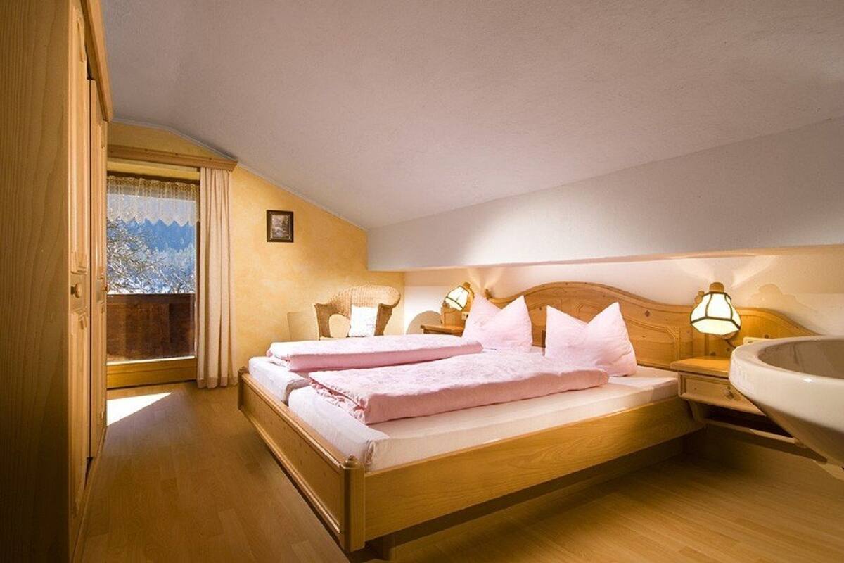 Een slaapkamer met een houten bed, twee nachtkastjes met lampen, een raam met gordijnen, en uitzicht op besneeuwde bergen.