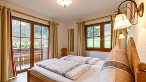Ein Schlafzimmer mit zwei Betten, großen Fenstern, einem hölzernen Kopfteil und einer Deckenleuchte.