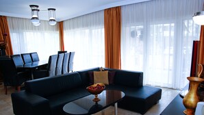 A modern living room with a black sectional sofa, a glass coffee table, and a dining area with a black table and chairs. - Princess Apartman (Siófok)