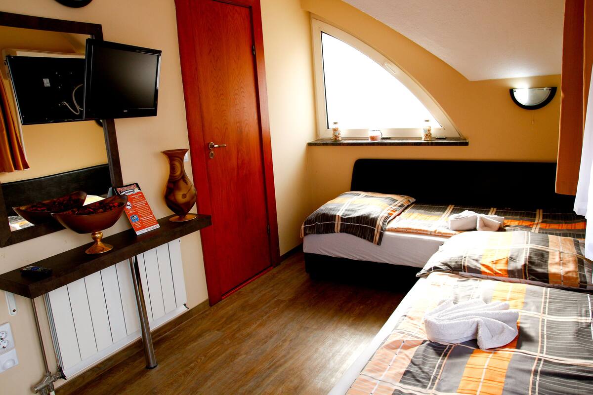 A hotel room with a bed, a TV mounted on the wall, a window, and a red door.