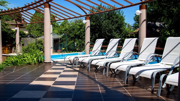 A poolside area with sun loungers, a pergola, and a tiled floor. - Princess Apartman (Siófok)