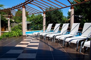 A poolside area with sun loungers, a pergola, and a tiled floor. - Princess Apartman (Siófok)