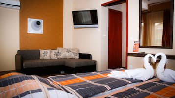 A hotel room with a sofa, a TV mounted on the wall, a mirror, and a bed with a decorative swan pillow arrangement.