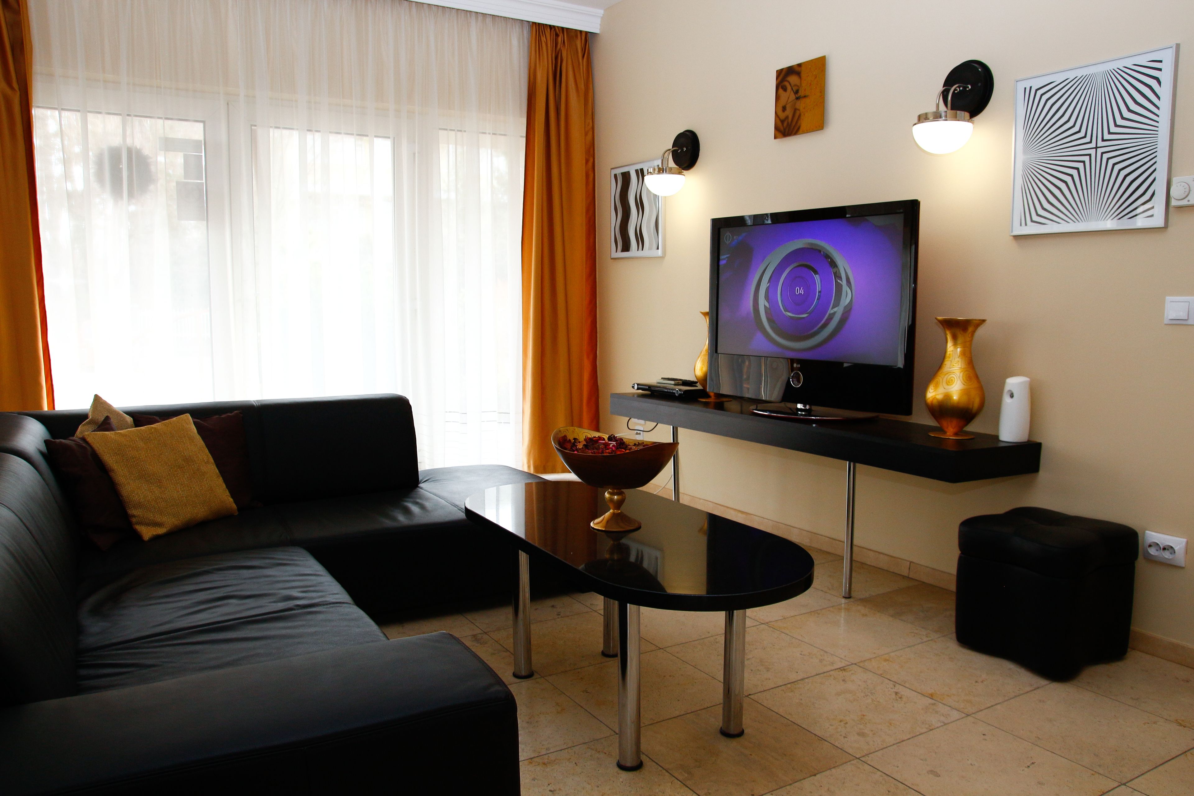 A modern living room with a black leather sofa, a glass coffee table, a flat-screen TV, and a decorative vase.
