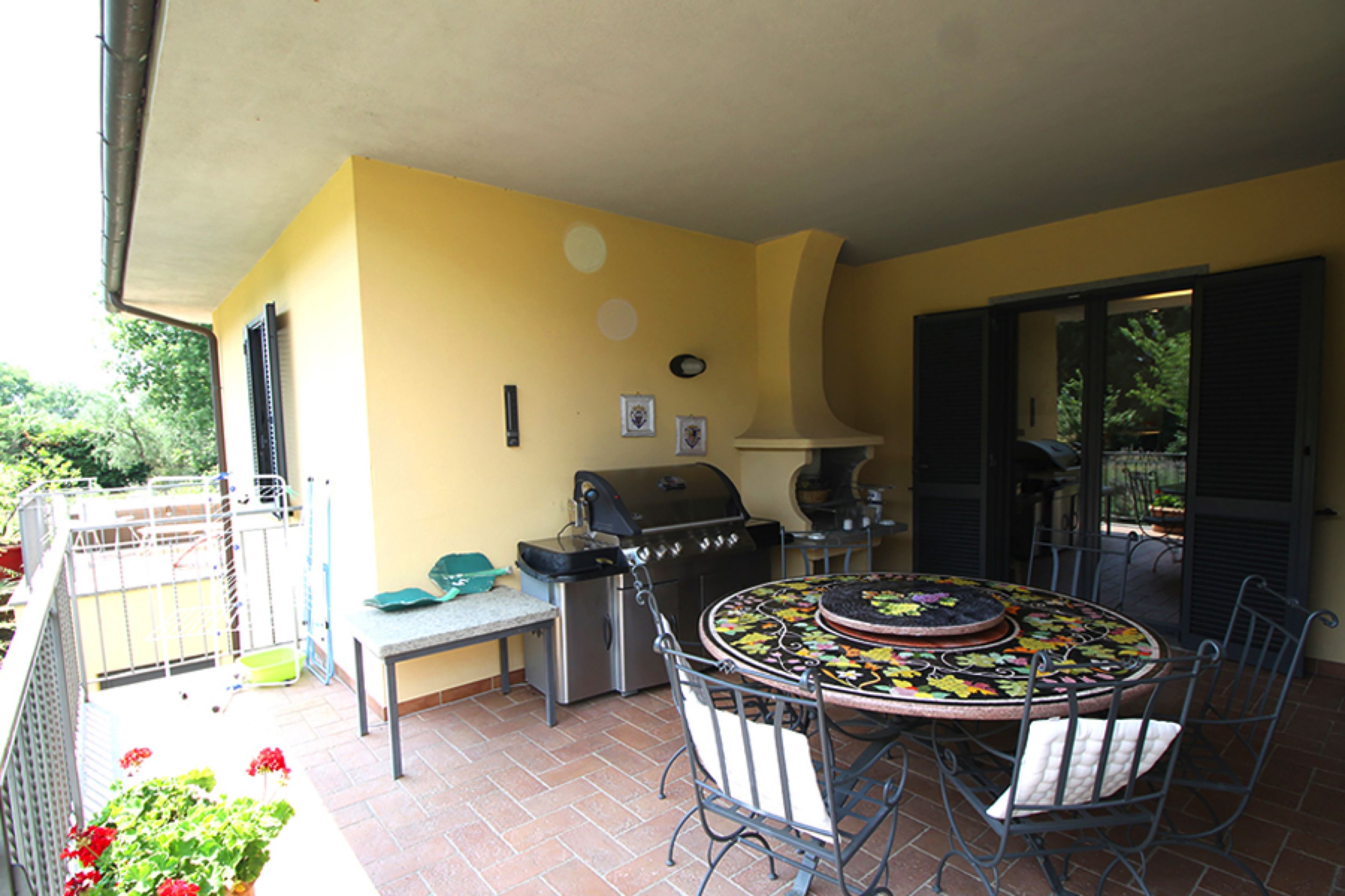 A patio with a grill, a table with chairs, and a view of the garden.