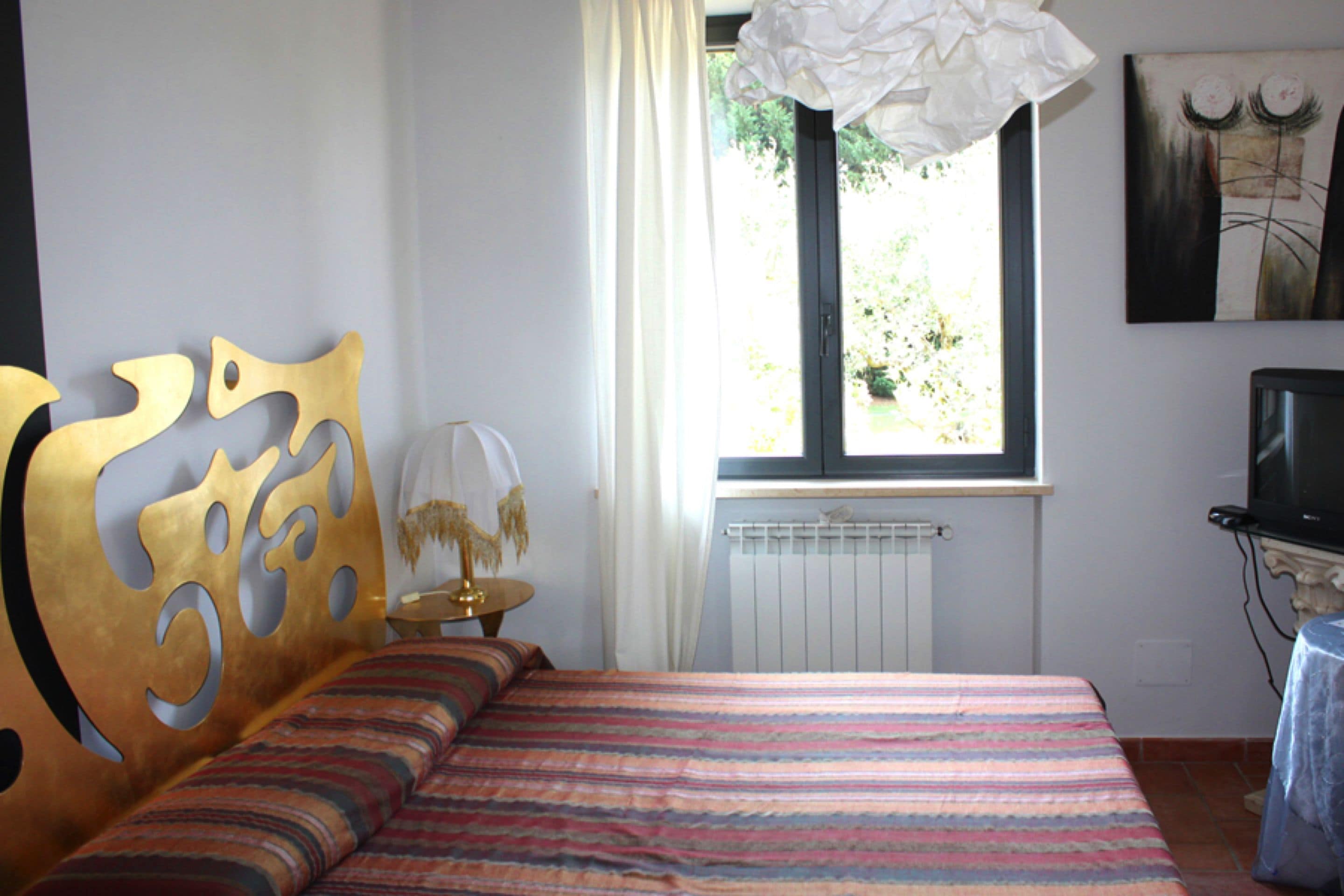 Una camera da letto con un letto, una finestra con tende, un termosifone, una televisione e un'opera d'arte appesa al muro.