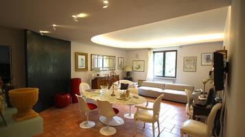 Een ruime woonkamer met een ronde eettafel, witte stoelen, een bank en een televisie.