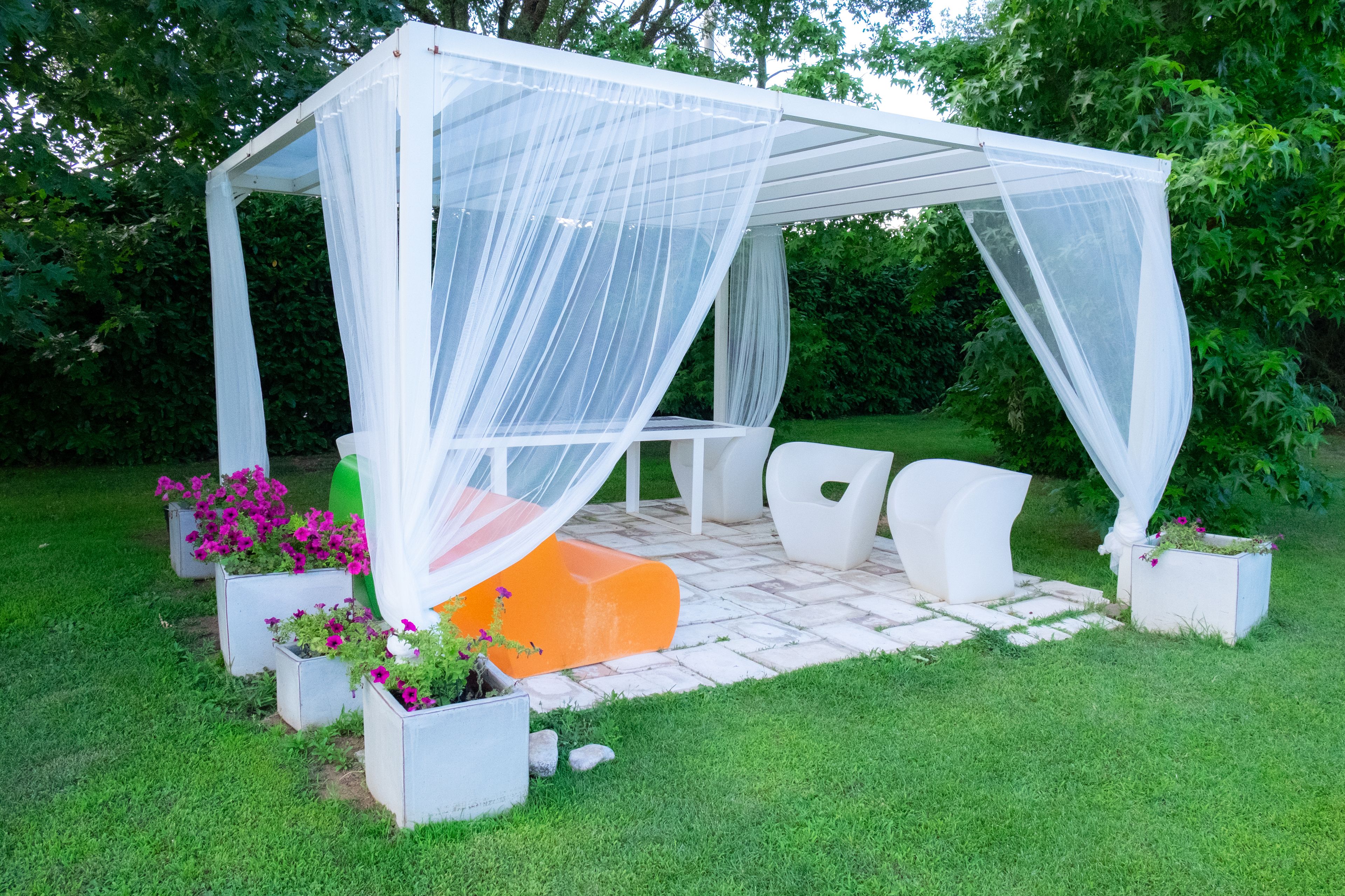 A covered outdoor seating area with a white canopy, white chairs, and planters with flowers.