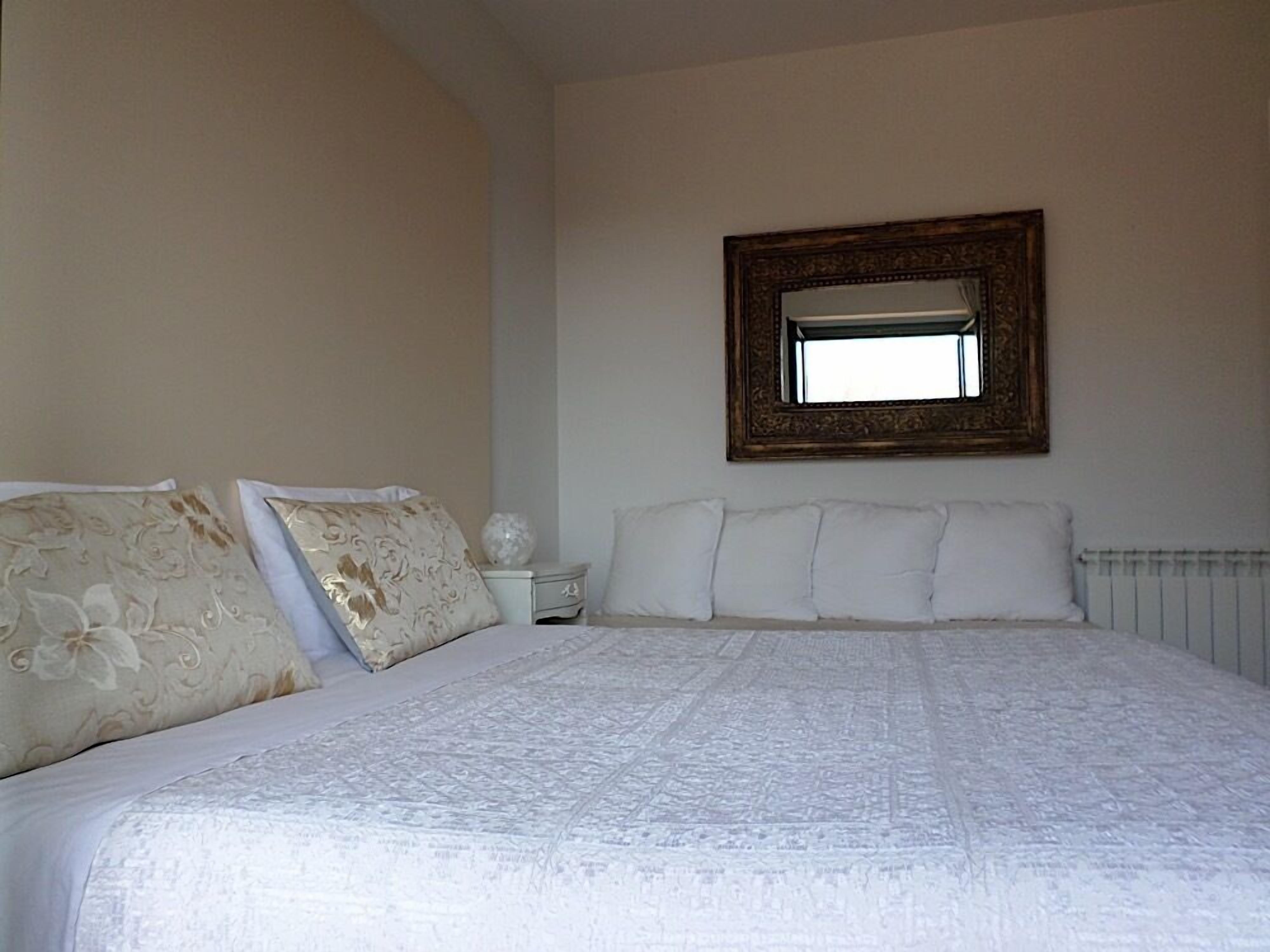 A bedroom with a large bed, white bedding, and a mirror on the wall.