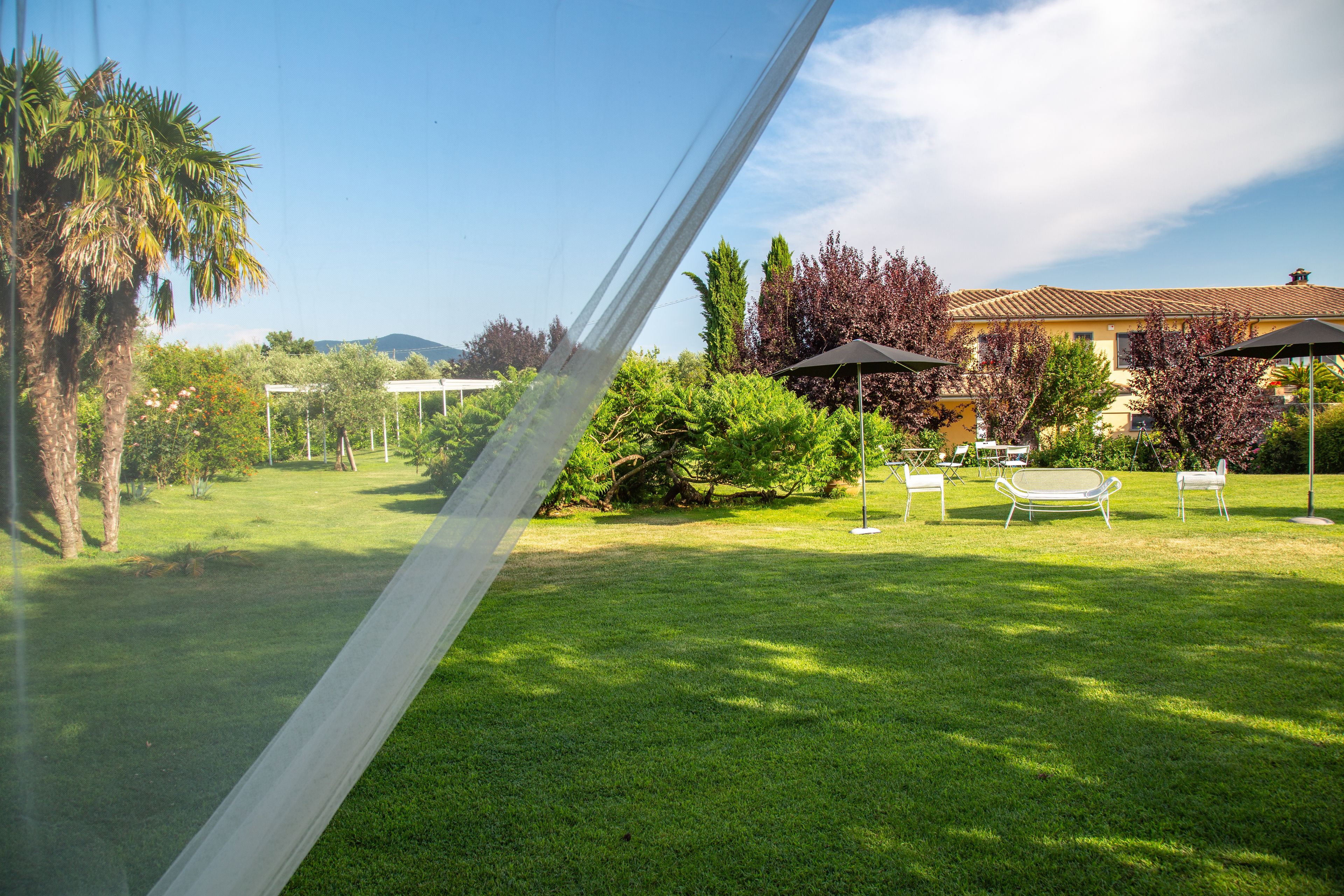 Un césped cuidado con mobiliario exterior, una pérgola y un edificio con techo de tejas al fondo.
