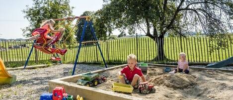 Un parque infantil con columpios, zona de juegos con arena y vehículos de juguete.