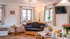 Una sala acogedora con un sofá, una mesa de comedor dispuesta para el desayuno y un televisor montado en la pared.