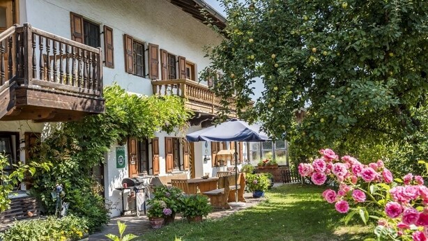 Un edificio de estilo europeo tradicional con balcón, mobiliario exterior y un jardín lleno de flores y plantas.