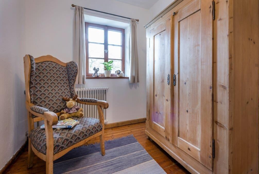 Une pièce chaleureuse avec une chaise en bois, un radiateur, une fenêtre avec des rideaux et une armoire en bois.