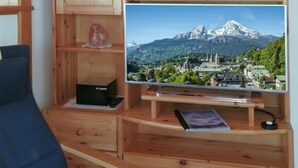 Puisesta materiaalista valmistettu viihdekeskus, jossa on litteänäyttöinen televisio, jolta näkyy kaunis vuoristomaisema, pieni hylly koriste-esineille ja laatikko kaukosäätimelle.