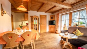 Een gezellige woonkamer met houten meubels, een eethoek met een tafel en stoelen, en een keuken met kasten en een televisie.
