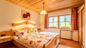 Een slaapkamer met een houten bed, een nachtkastje, een raam met gordijnen en een radiator.