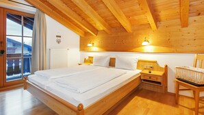 A wooden bedroom with a large bed, two bedside tables, a chair, and a window with curtains.