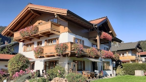 A two-story chalet with wooden balconies, flower boxes, and a garden with outdoor seating.