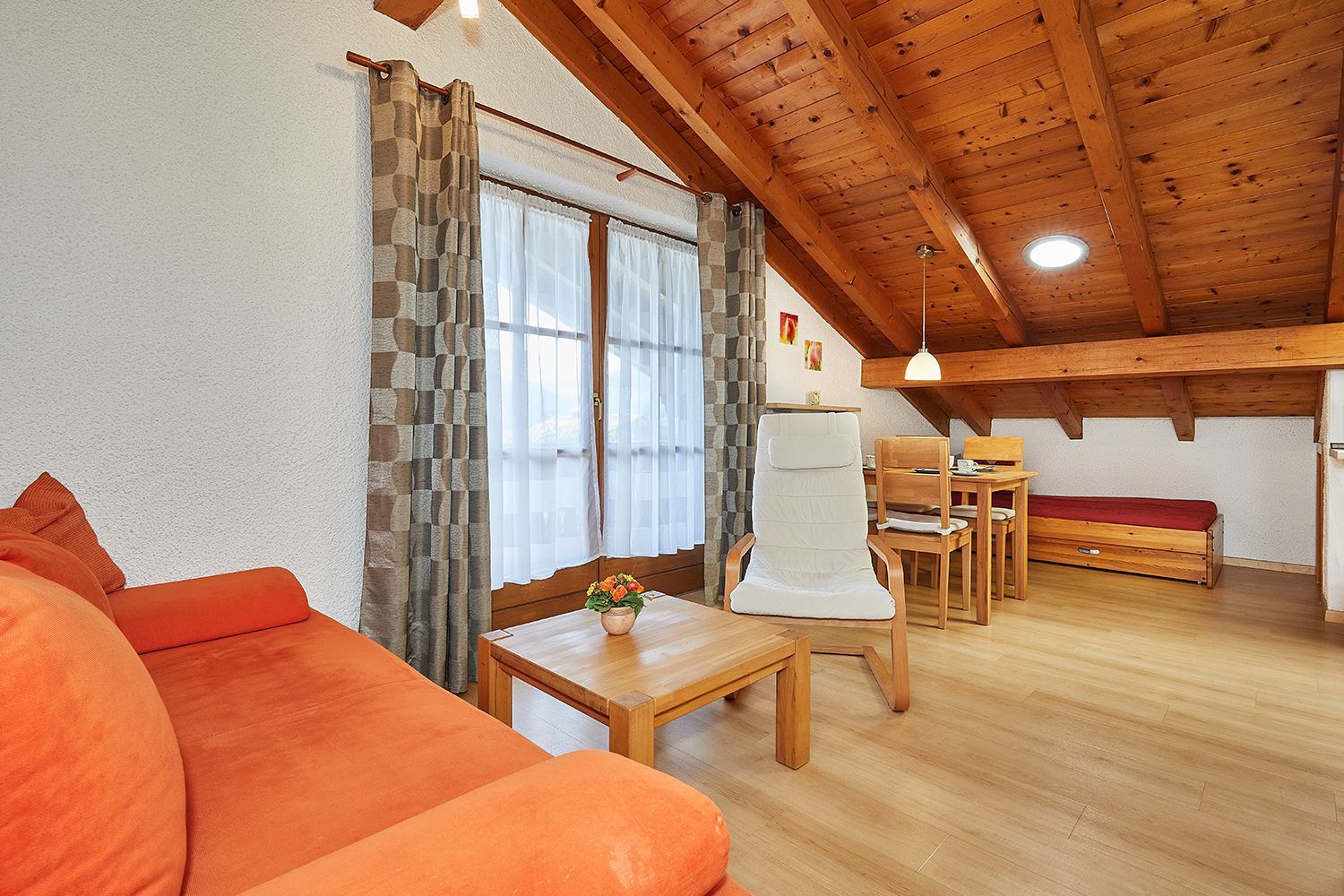 Uma sala de estar acolhedora com teto de madeira, um sofá, uma mesa de jantar e uma cadeira.