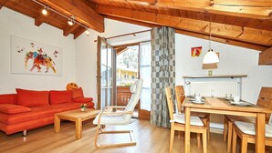 Een gezellige woonkamer met een rode bank, een houten salontafel en een eethoek met een houten tafel en stoelen.