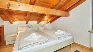 Een slaapkamer met een houten plafond, een bed met kussens en handdoeken, een nachtkastje en een bijzettafeltje.