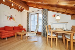 Un salon chaleureux avec un plafond en bois, un canapé rouge, un fauteuil blanc et une table à manger avec des chaises.